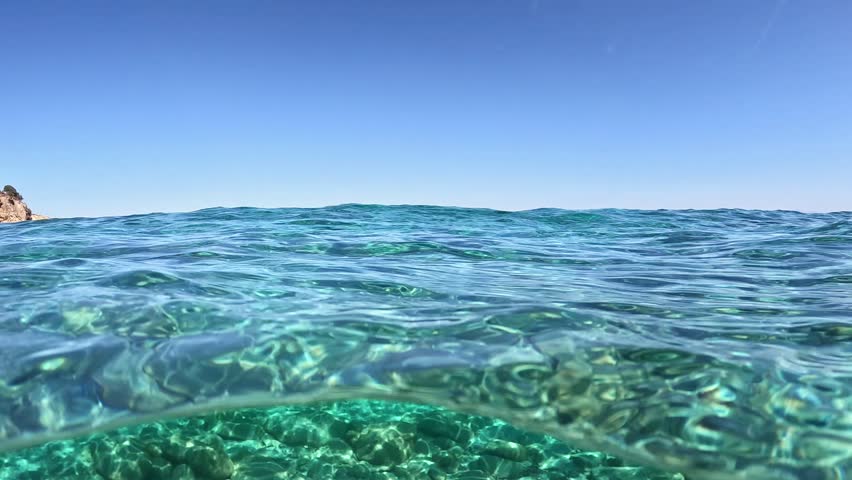 Over under view of crystal clear Mediterranean Sea water on sunny day, transparent water surface shows seabed under blue sky. Crystal clear Mediterranean Sea water split level view