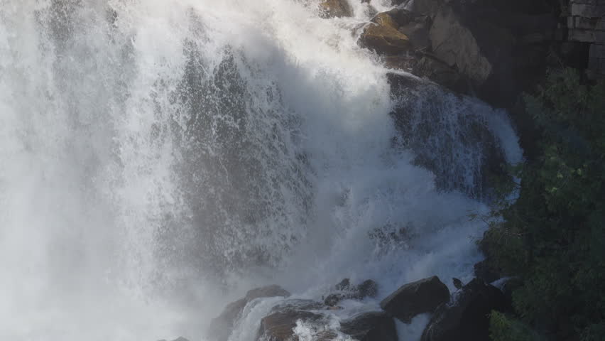 A heavy volume of water surges down the rocky cliff side of Inglis Falls during spring. The rushing white water pounds against dark limestone boulders in Owen Sound, Ontario.