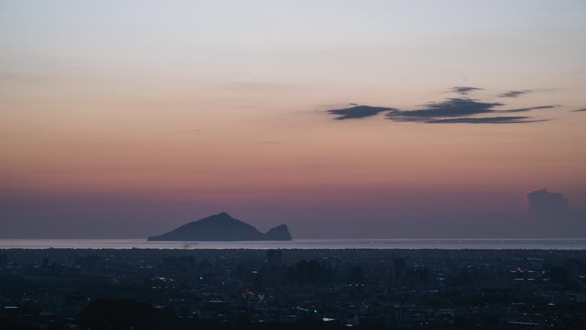 Breathtaking sunrise view over Yilan City and Turtle Island in Taiwan, featuring colorful morning sky clouds, ocean waters, and fading city lights.