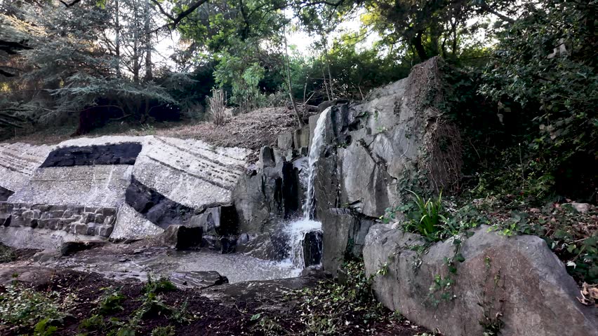 Clear water flowing down a small artificial waterfall in a tranquil public park setting.