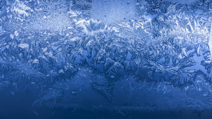 Frost crystal patterns forming intricate geometric shapes on glass in extreme winter cold