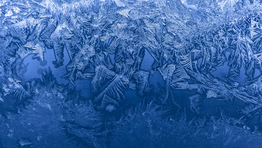 Frost crystal patterns forming intricate geometric shapes on glass in extreme winter cold