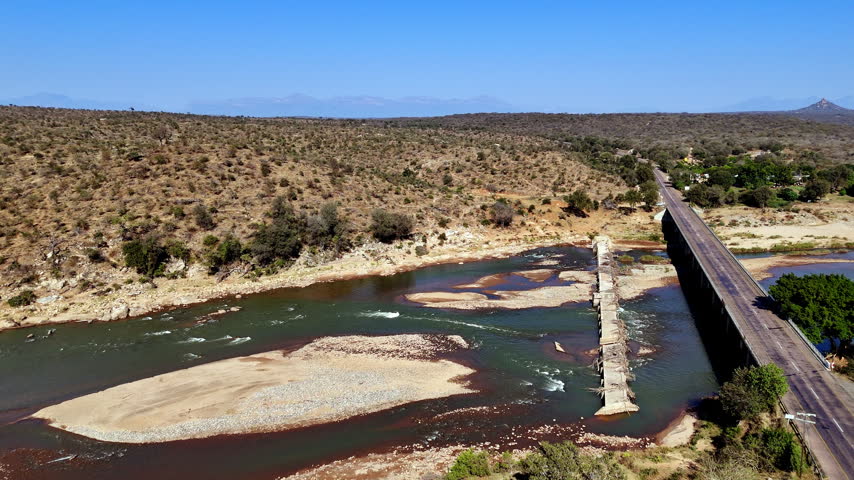Tarred road bridge next to old unused small bridge spanning African river. Drone