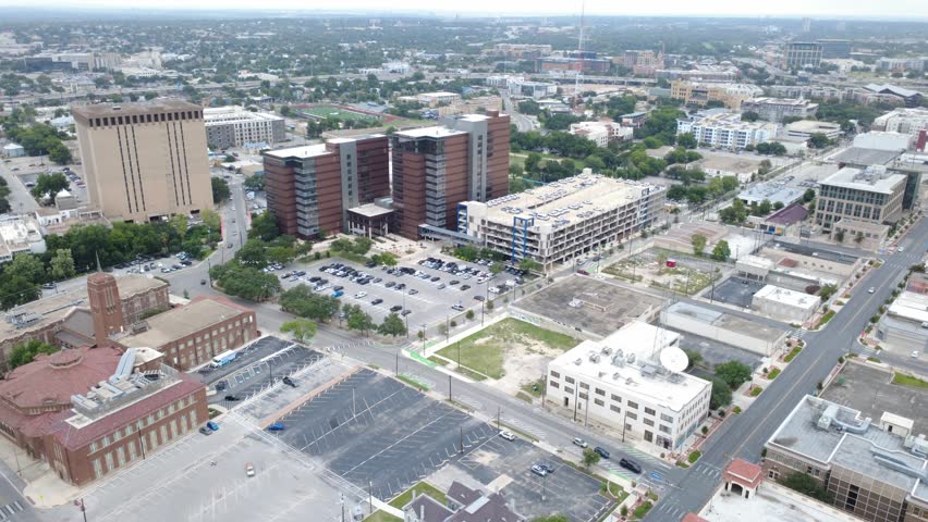 Downtown business district asphalt lots intersect structured parking facilities near corridors. Multi-story office buildings overlook municipal thoroughfares in historic San Antonio, Texas. USA