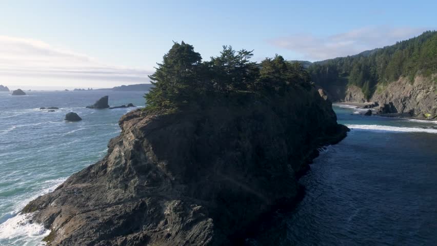 A forward-rising drone shot, flying-low over a massive sea-stack, revealing a series of sea stacks and the Pacific coastline, near 