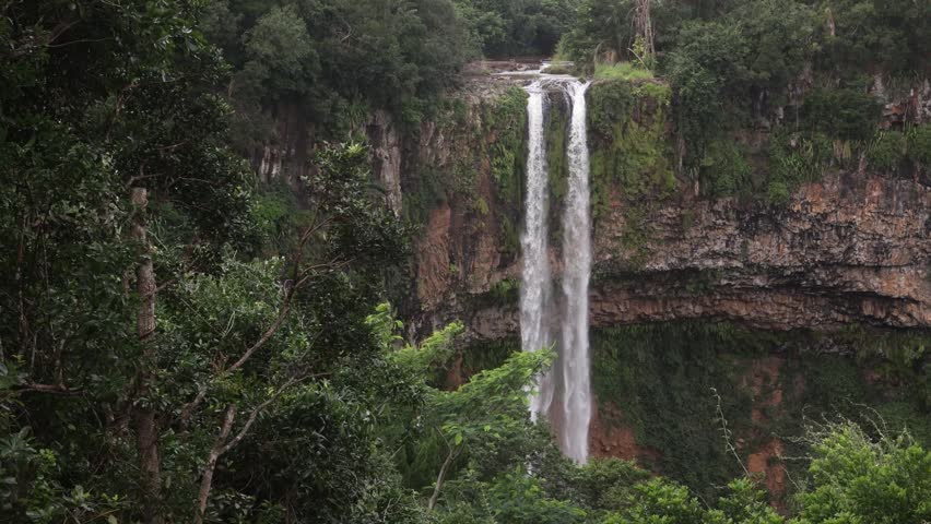 Alexandra Falls plunging down a lush green cliffside in the mountainous national park of Mauritius, showcasing a remote tropical cascade surrounded by dense rainforest foliage.
