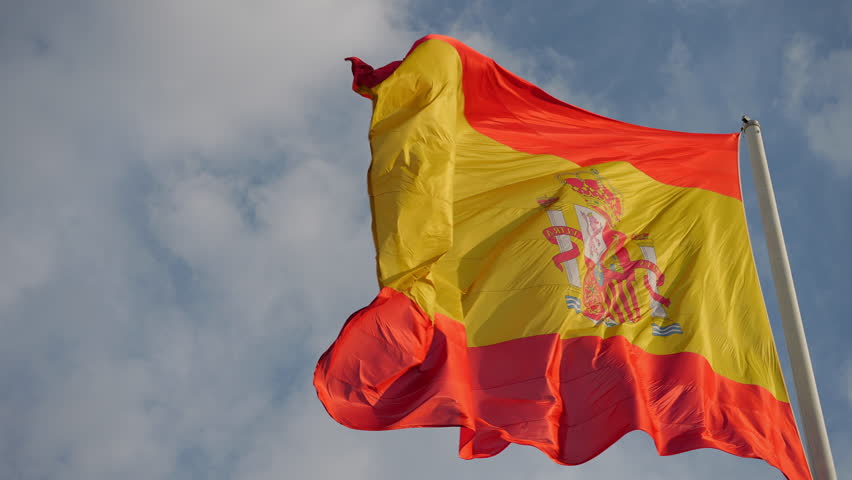 Red and yellow Spanish flag with the coat of arms flying majestically in the breeze. A powerful symbol of national pride and identity