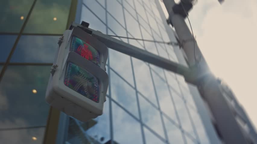 Red pedestrian traffic signal in Tokyo, Japan, indicating do not walk, with a modern glass skyscraper reflecting the sky and clouds in the background on a sunny day with lens flare