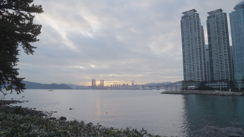 A boat sails across the water as the Sun Sets over Gwangan Bridge in the Background