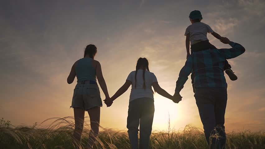 Father walking in field child on shoulders. Boy and girl enjoy sunset with family. Walking hand in hand brings happiness. Family time at sunset shows joy. Child smiles as father shares this moment.