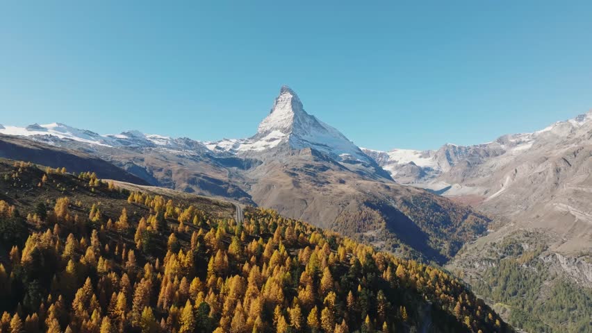 Aerial drone view of the Matterhorn mountain peak rising above a colorful autumn forest in Switzerland on a bright sunny day. Alpine autumn landscape.