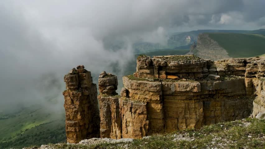 A dramatic landscape shot showing dense fog and clouds drifting over massive red rock pillars and steep canyon cliffs on a overcast day.