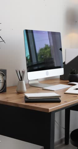 Wooden table with computer, stationery and chair near white wall in home office, camera moving right. Interior design