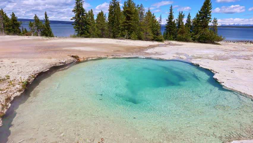 Steam rises above the vivid blue waters of Black Pool with Yellowstone Lake in the background at West Thumb Geyser Basin