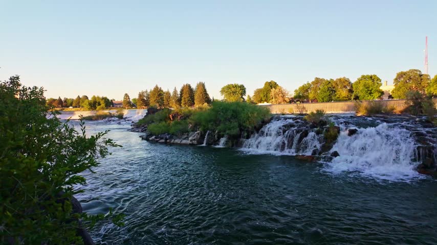 Historic Idaho Falls water tower stands above the Snake River as water cascades over the falls in golden light