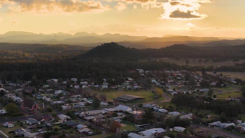 Wide aerial shot of a rural town and mountains during golden hour in Coonabarabran, Australia.