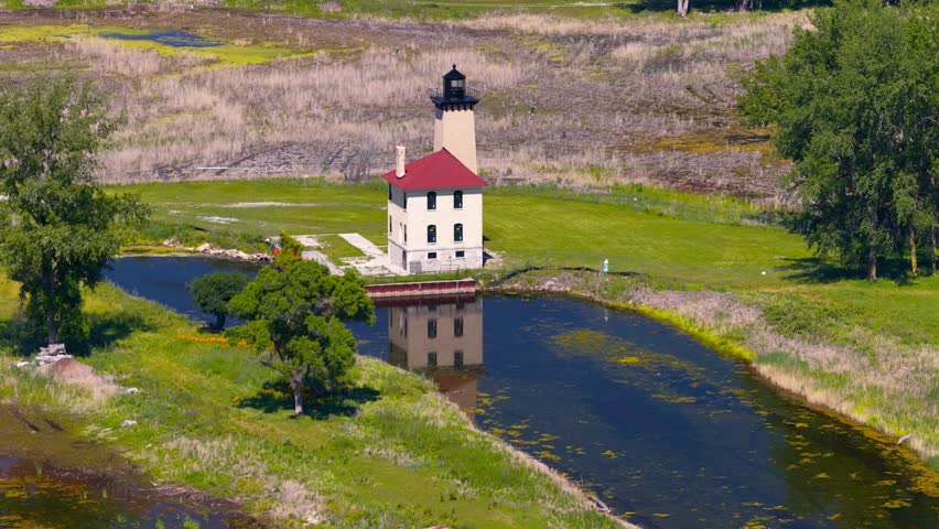 Saginaw river range Lighthouse standing by a winding channel, surrounded by green trees and grass by Lake Huron.