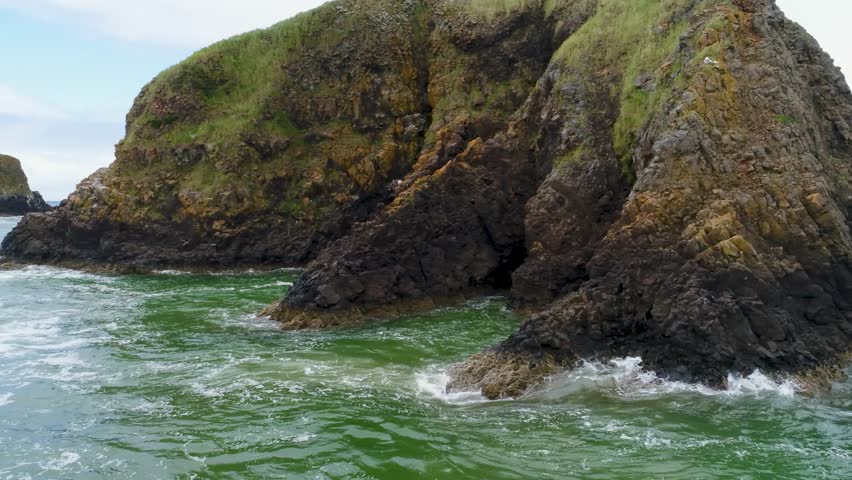Cinematic drone rises from ocean level to orbit two hikers atop Bird Rocks off John Yeon State Natural Site, revealing Oregon’s rugged coast with distant Haystack Rock near Cannon Beach.