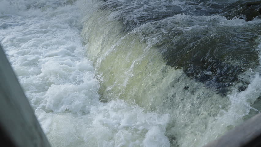A high-angle perspective shows the forceful flow of the Sauble River cascading over rocky ledges. The rapid spring current churns into thick white foam and misty spray.