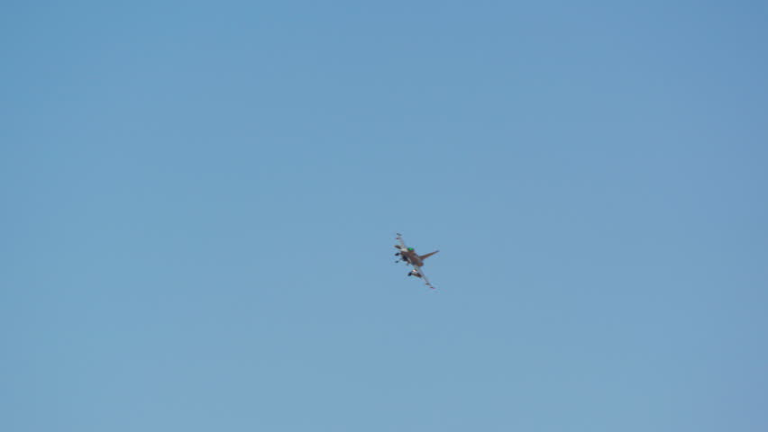 Military fighter jet approaching for landing with its landing gear extended, flying against a clear blue sky in slow motion