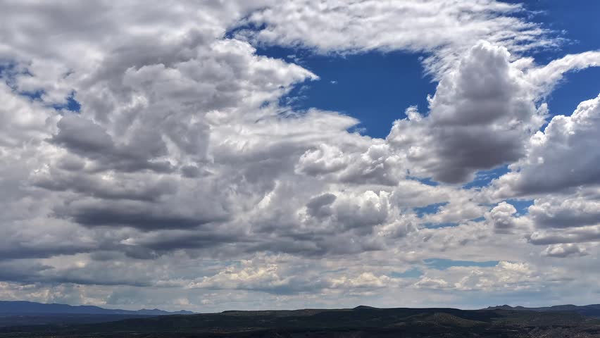4K drone timelapse capturing a beautiful, vast sea of fast-shifting clouds over a dark Southwest high desert landscape. Patches of bright blue sky break through the dense rolling cloudscape.