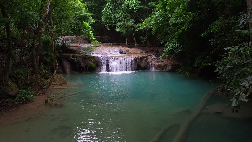 A waterfall with clear blue water, surrounded by natural rock formations and lush trees.