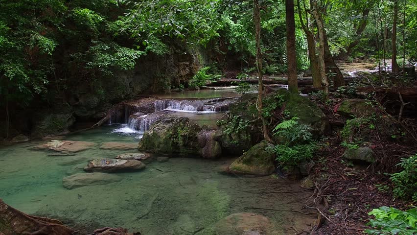 A waterfall with clear blue water, surrounded by natural rock formations and lush trees.