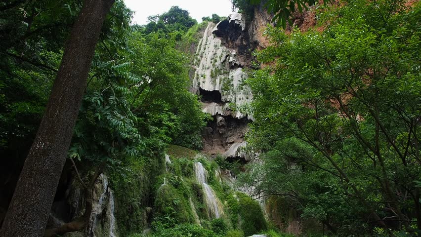 A waterfall with clear blue water, surrounded by natural rock formations and lush trees.