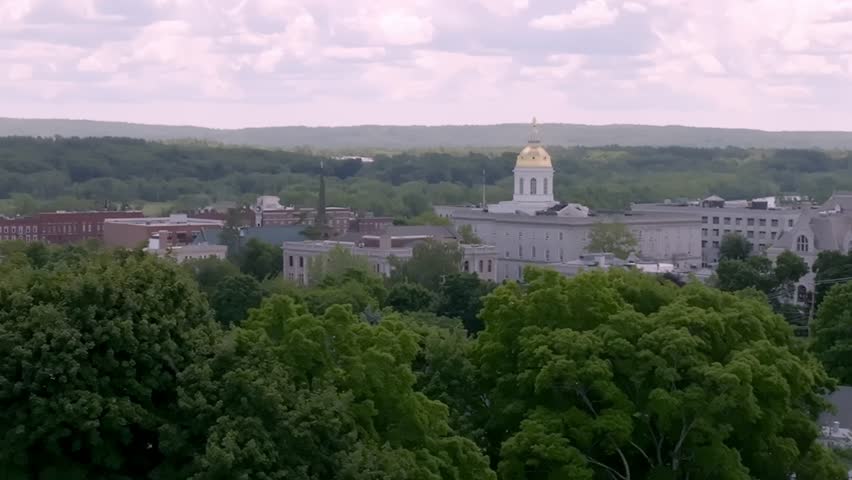 Aerial drone footage of the New Hampshire State Capitol in Concord as the camera moves smoothly from right to left, showcasing the historic gold-domed government building and surrounding downtown city