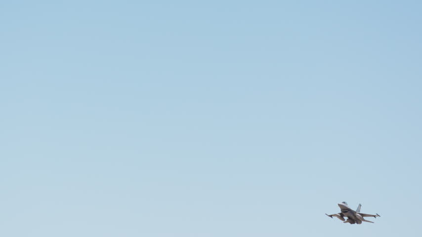 A military fighter jet ascends through a clear blue sky in slow motion, soaring upwards during a daytime flight