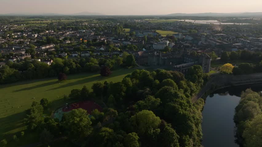 A cinematic aerial shot showcasing the historic Kilkenny Castle and the winding River Nore during a beautiful sunset in Ireland. Highquality footage for travel and heritage documentaries.