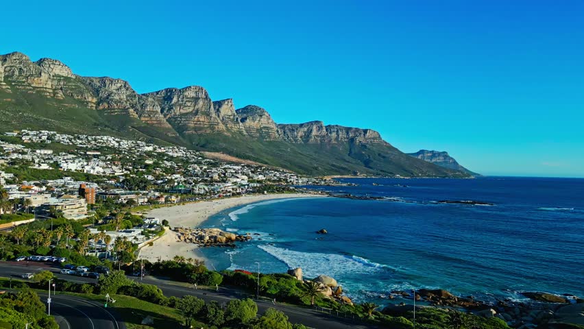 Cinematic wide aerial view, Camps Bay and Cape Town, South Africa, with Table Mountain rising above the Atlantic coastline, beaches and Summer coastal scenery