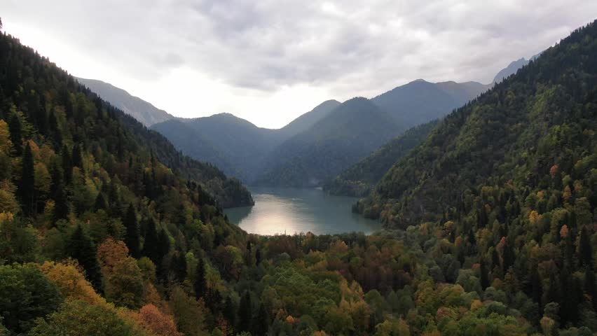 Aerial view of the scenic Lake Ritsa nestled among autumn forests and high mountains in Abkhazia under a cloudy sky.