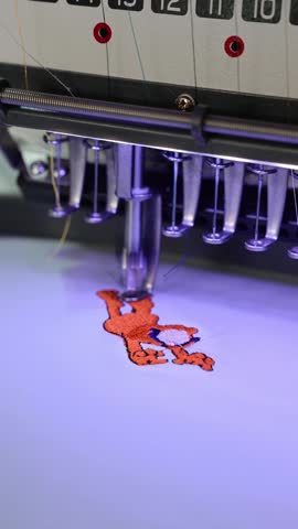 Automated sewing machine embroidering a cartoon tiger patch on white fabric in a textile factory
