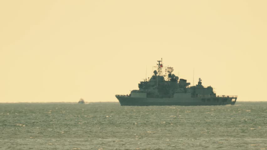 Naval ship sailing on the water during sunset near the coastline