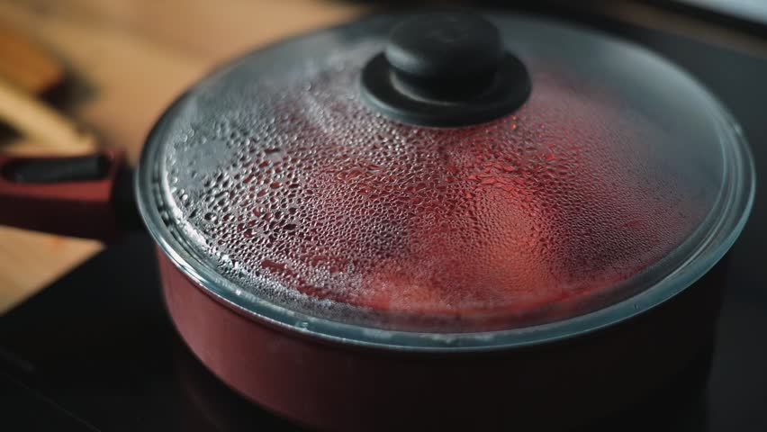 A covered pot sits on a stove, steam rising from its lid as food cooks inside. The kitchen environment shows various tools and a warm ambiance during meal preparation.