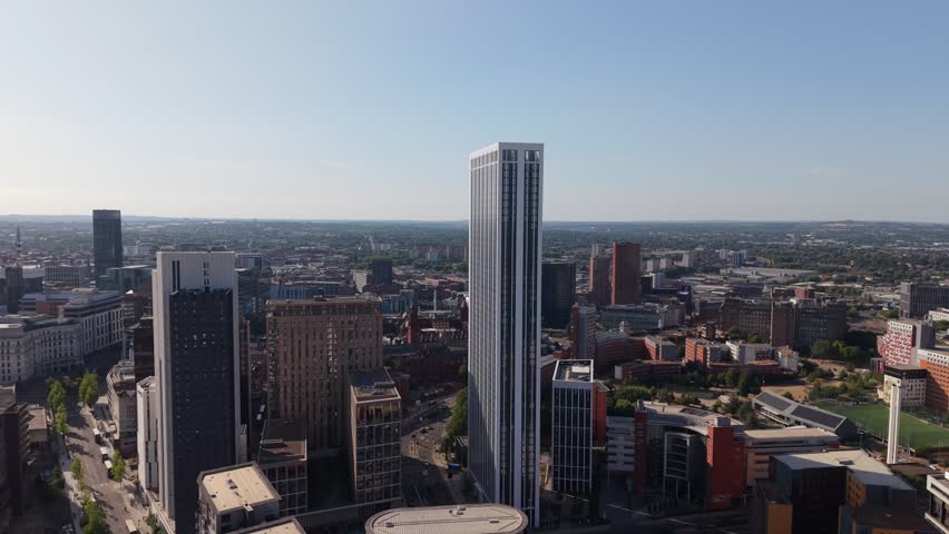 Drone aerial view of Birmingham city centre featuring a modern skyscraper rising above the skyline, surrounded by contemporary office buildings and urban development under clear summer skies.
