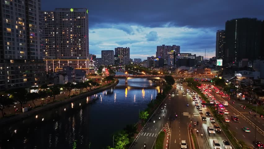 A vibrant nighttime cityscape along Vo Van Kiet Boulevard in Saigon, featuring flowing traffic, illuminated buildings, a canal, bridge, and reflections.