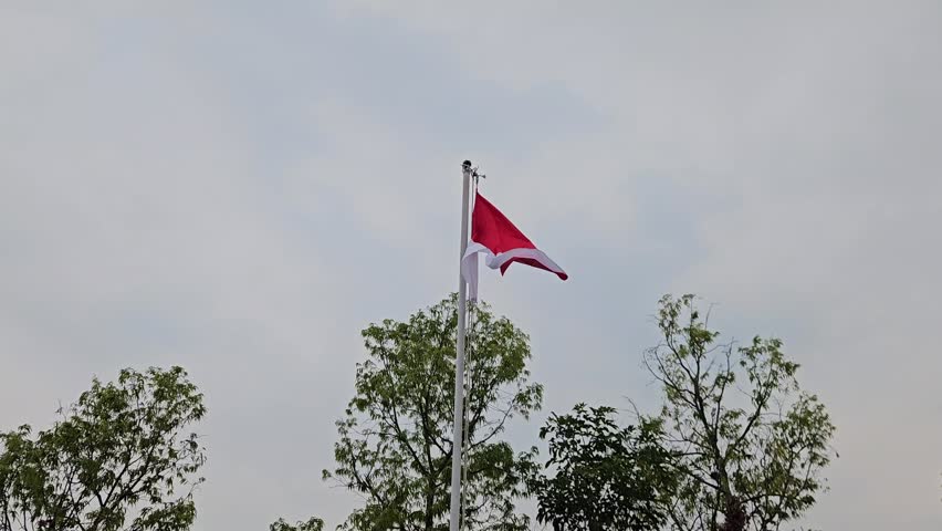 Central Java, July 31, 2026. The red-and-white Indonesian flag fluttering in the countryside as dusk falls.