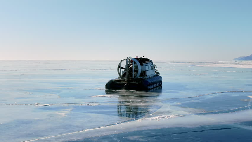 Hovercrafts moving over thin ice on frozen Baikal lake. Amphibious vehicle sliding, winter transport. Arctic transportation, extreme travel exploration in cold climate landscape. Mountains background.