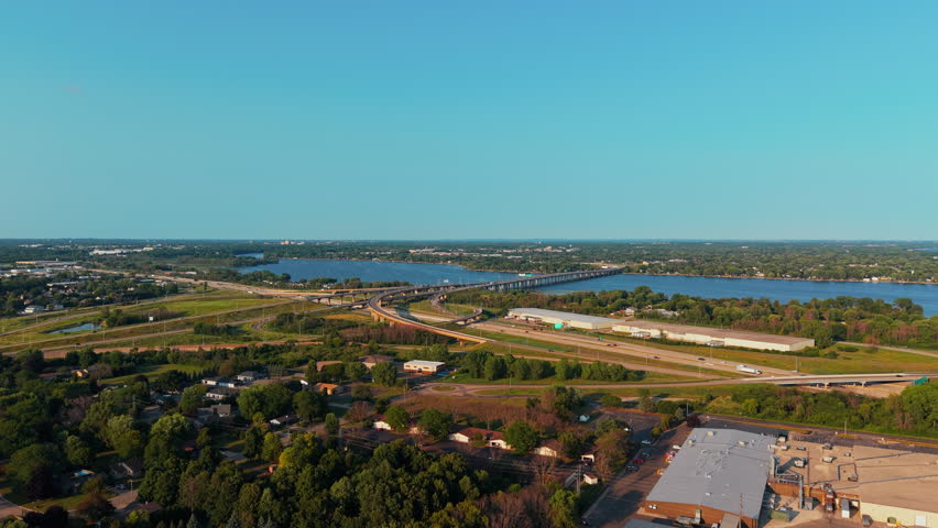 Aerial establishing shot of cars traveingl across a long Fox River bridge and curving highway 41 interchange beside a suburban neighborhood Neenah, Wisconsin