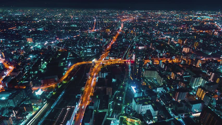 Osaka cityscape nocturnal aerial timelapse showing fast moving vehicle light trails weaving through an illuminated modern metropolis filled with towering residential and office buildings