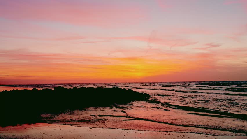 Serene Beach Sunset Landscape with Silhouetted Rocks and Gentle Ocean Waves
