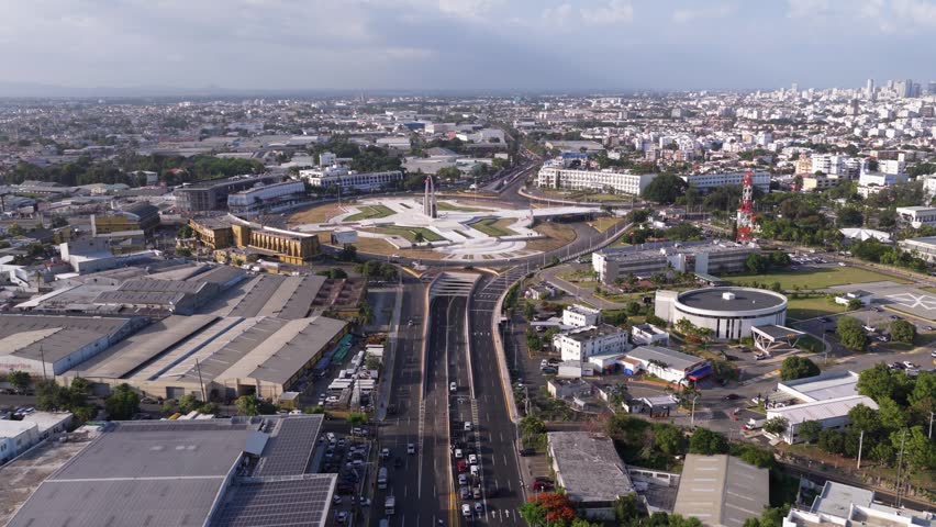 Large cross shaped Plaza de la Bandera monument and roundabout surrounded by city buildings in Santo Domingo, Dominican Republic. Aerial forward