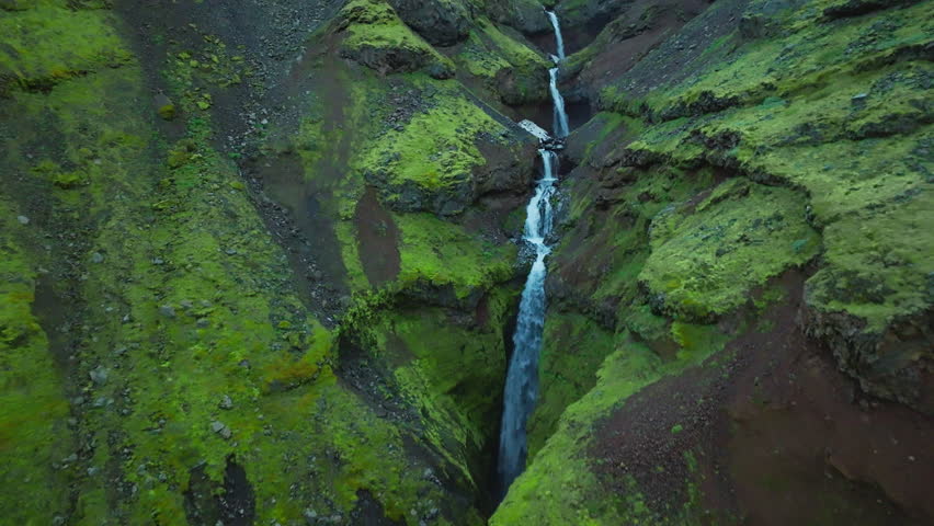 Cinematic drone flight through the lush Mulagljufur Canyon revealing towering moss-covered cliffs, cascading waterfalls and a winding river deep within Iceland’s spectacular Highlands.
