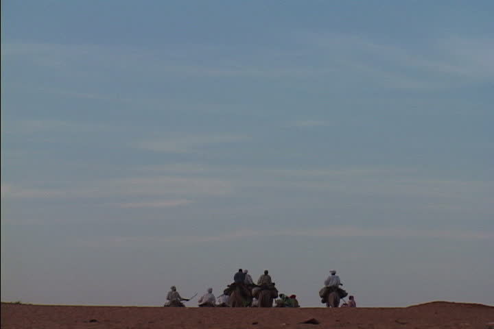 ABU SHOUK AND KABKABIYA, NORTH DARFUR, SUDAN - NOVEMBER 11, 2004: Men on camels and donkeys ride off into the distance. Two goats run past in foreground.
