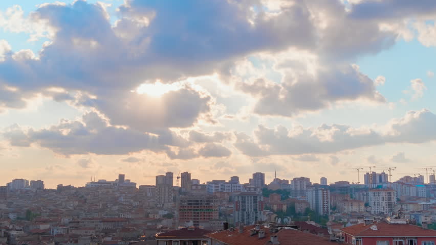 Timelapse: setting sun rays shine through fast moving clouds over Istanbul residential buildings in a wide angle sunset view. The city gets darker under orange evening sky - time lapse