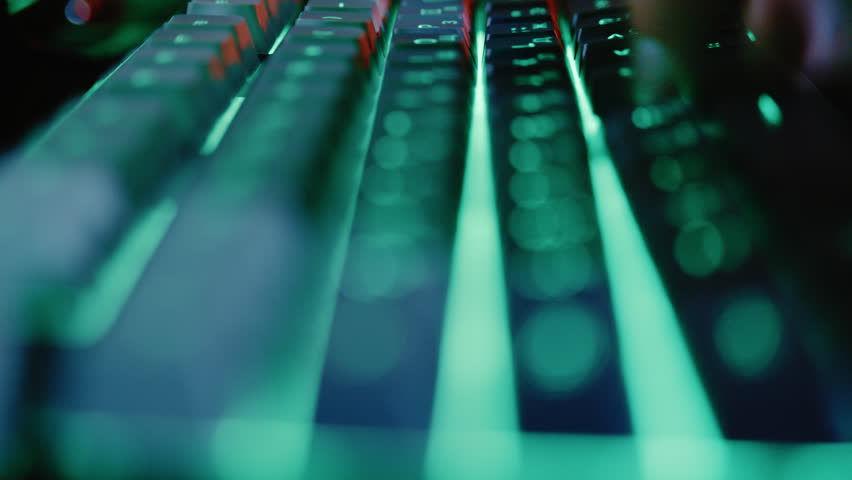 Close-up view of a programmer or gamer typing quickly on a keyboard with green neon backlight