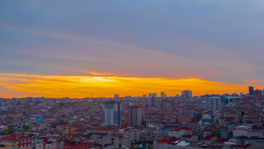 Timelapse: setting sun is coloring dense clouds red over Istanbul after rain as the city gets darker. Residential buildings below the red afterglow - time lapse