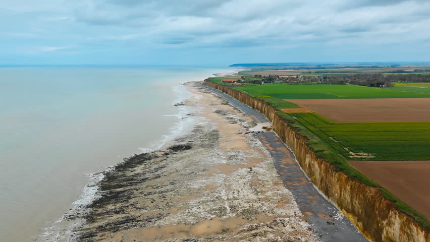 Aerial view of Normandy chalk coastline with farmland above English Channel. Coastal erosion and rural land near shoreline
